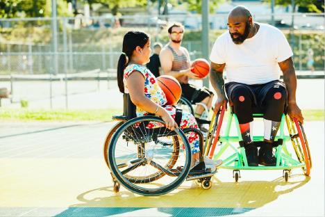 Smiling young female learning how to play wheelchair basketball from her coach on a sunny afternoon. [The Disability Collection / Getty Images] 
